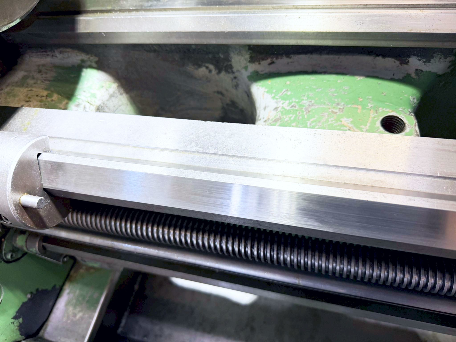Close-up of a polished aluminum linear rail and ball-screw assembly on a green industrial machine.